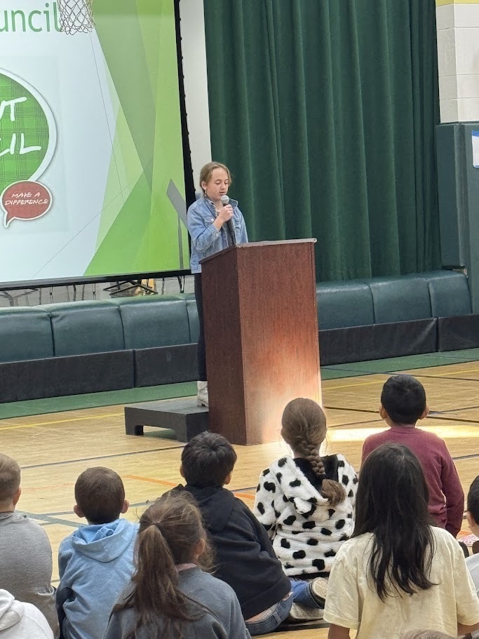 Image of a student speaks into a microphone behind a podium to deliver a speech