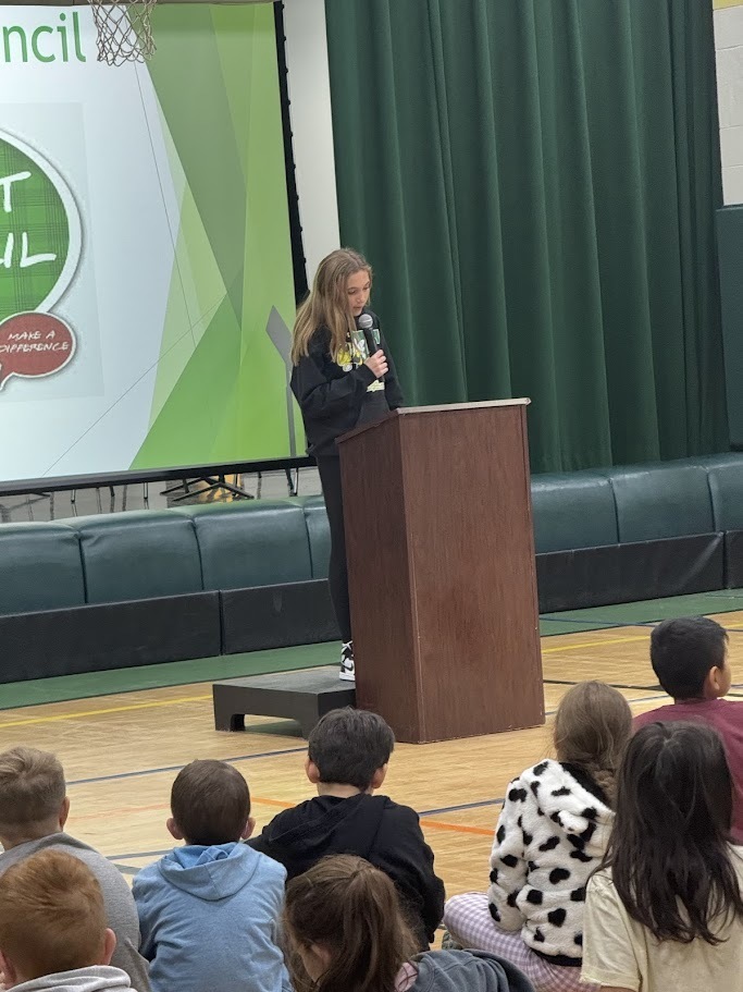 Image of a student speaks into a microphone behind a podium to deliver a speech