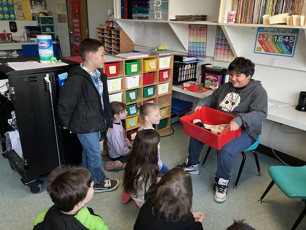Image of a student holding a guinea pig in a red bin with other students sitting in front of him