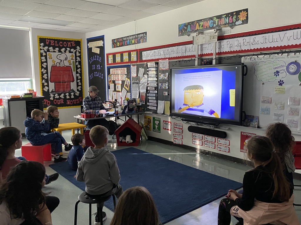 Image of a 4th grade class sitting in front of a smartboard looking at a story that is being projected from a document camera