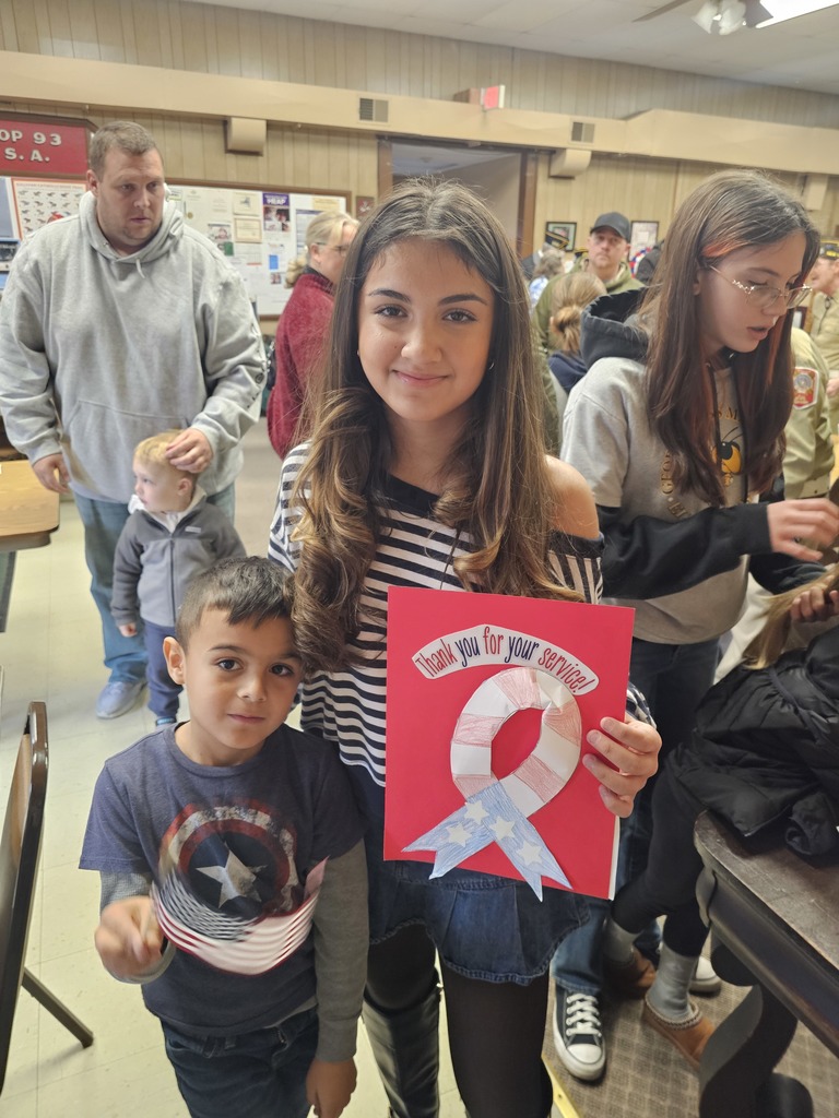 Two students pose for the camera, one with a hand-held American Flag the other with a poster the says "Thank you for your service"