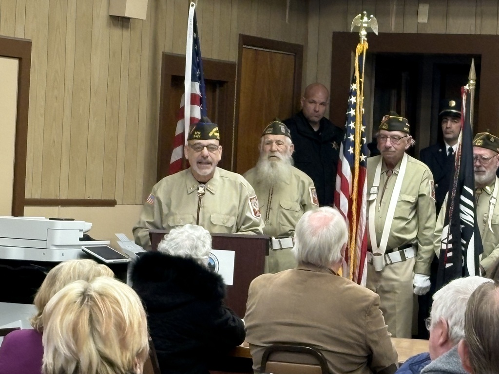 A uniformed veteran speaks to the crowd from behind a podium at a Veterans Day event