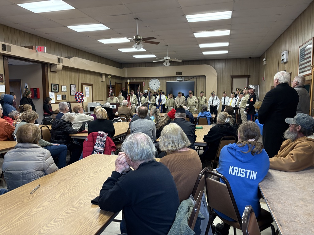 Attendees at a Veterans Day event sit in the foreground while you can see uniformed service men in the background