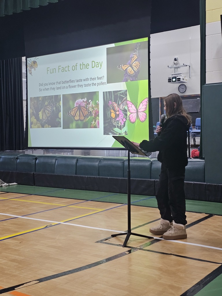 Image of a student standing at a microphone in front of a media screen that reads "Fun Fact of the Day"
