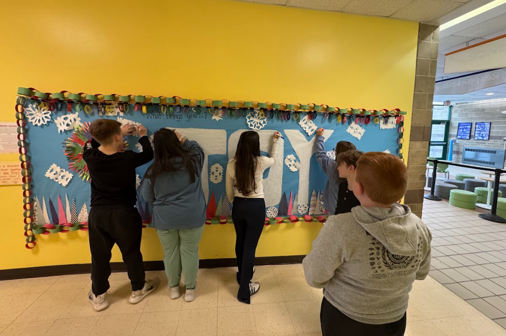 Image of students writing what bring them joy on a bulletin board they created