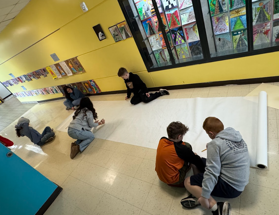 Student sit on the floor to plan out a bulletin board