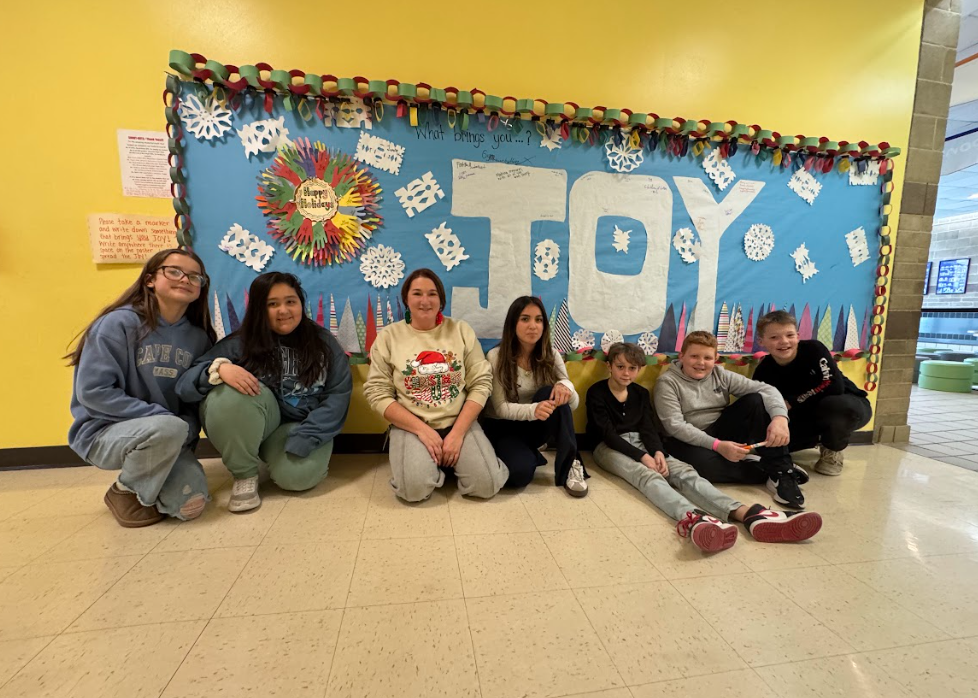 Image of students and a teacher sitting in front of a bulletin board they created