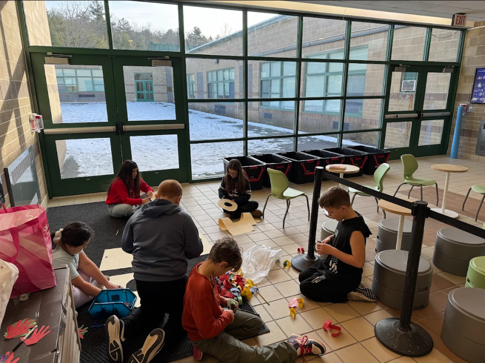 Image of students sitting on the floor working on pieces which will hang on a bulletin board
