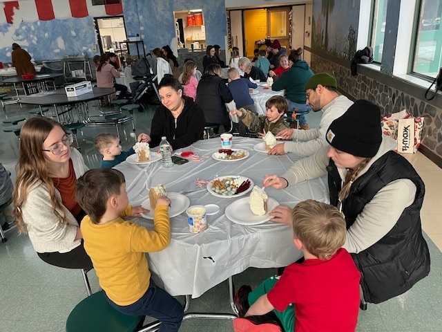 Families sit at tables and make gingerbread houses during a school event