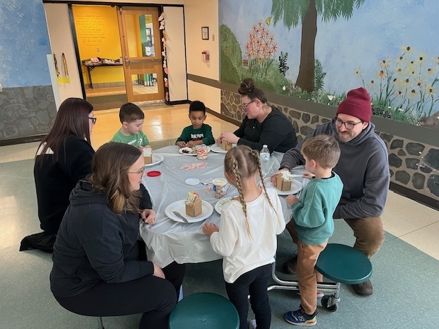 Families sit at tables and make gingerbread houses during a school event