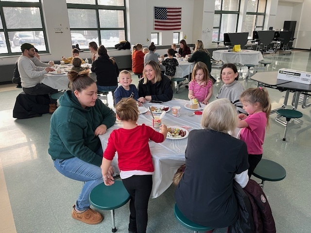 Families sit at tables and make gingerbread houses during a school event