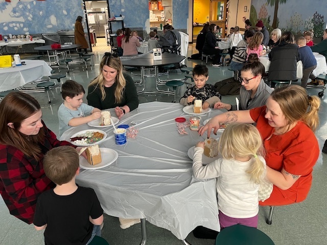 Families sit at tables and make gingerbread houses during a school event
