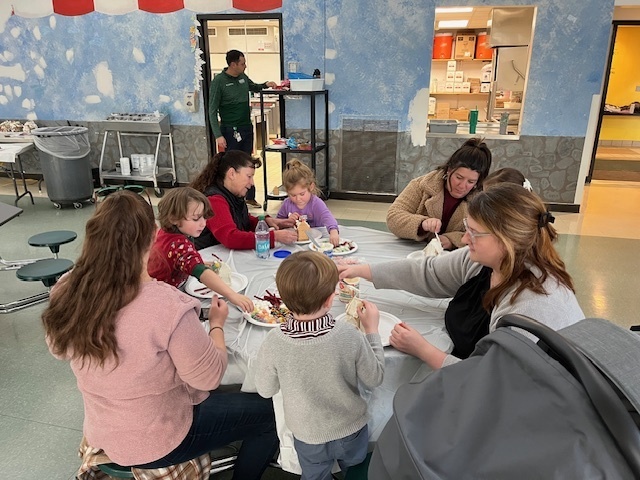 Families sit at tables and make gingerbread houses during a school event