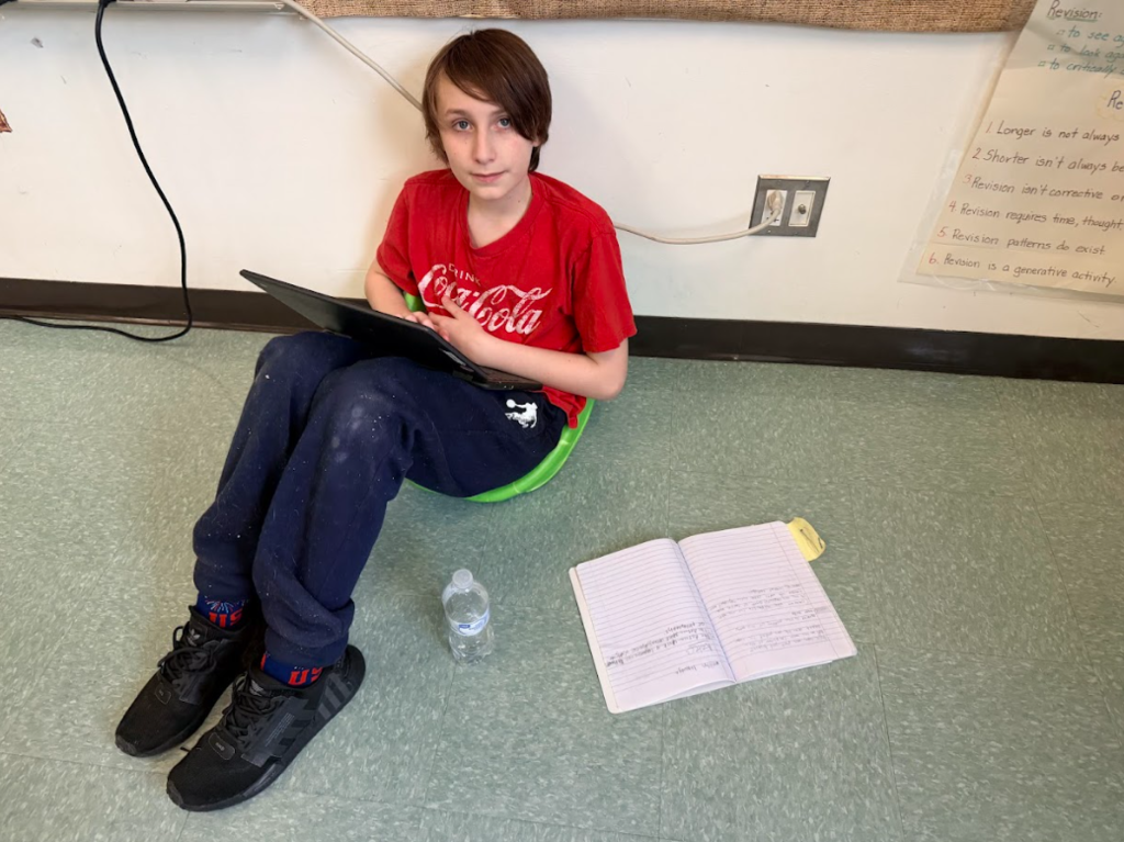 Image of student sitting on the floor with his chromebook