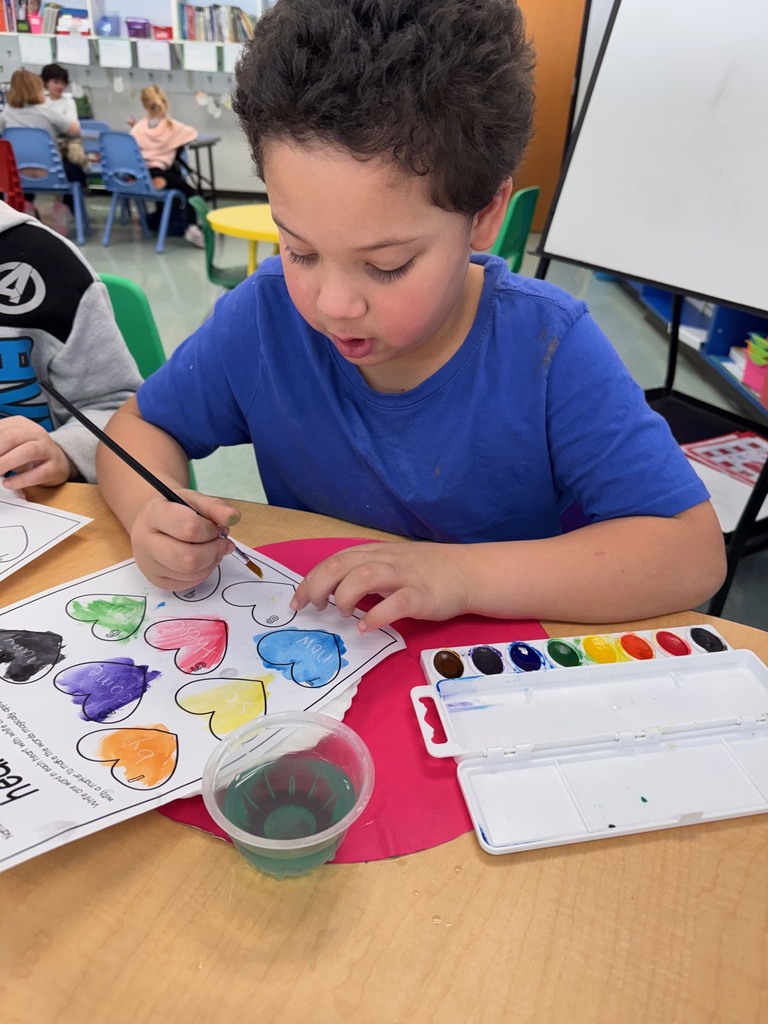 A student is seen with a paintbrush painting their "heart" words worksheet