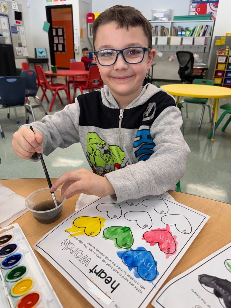A student is seen with a paintbrush painting their "heart" words worksheet