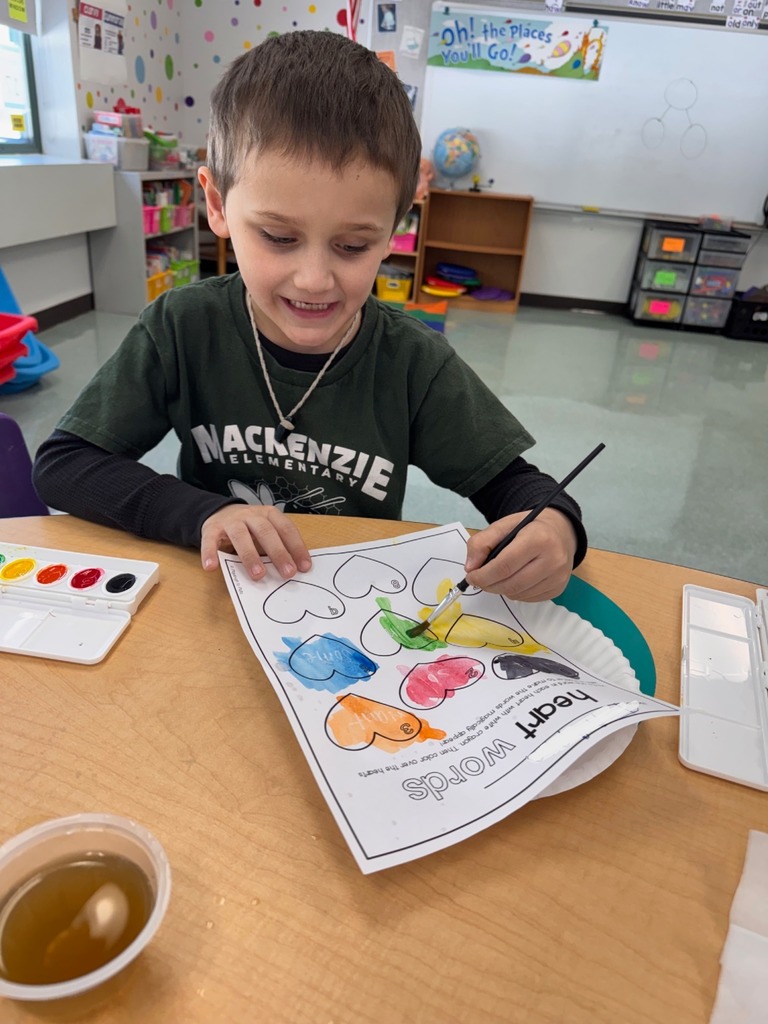 A student is seen with a paintbrush painting their "heart" words worksheet