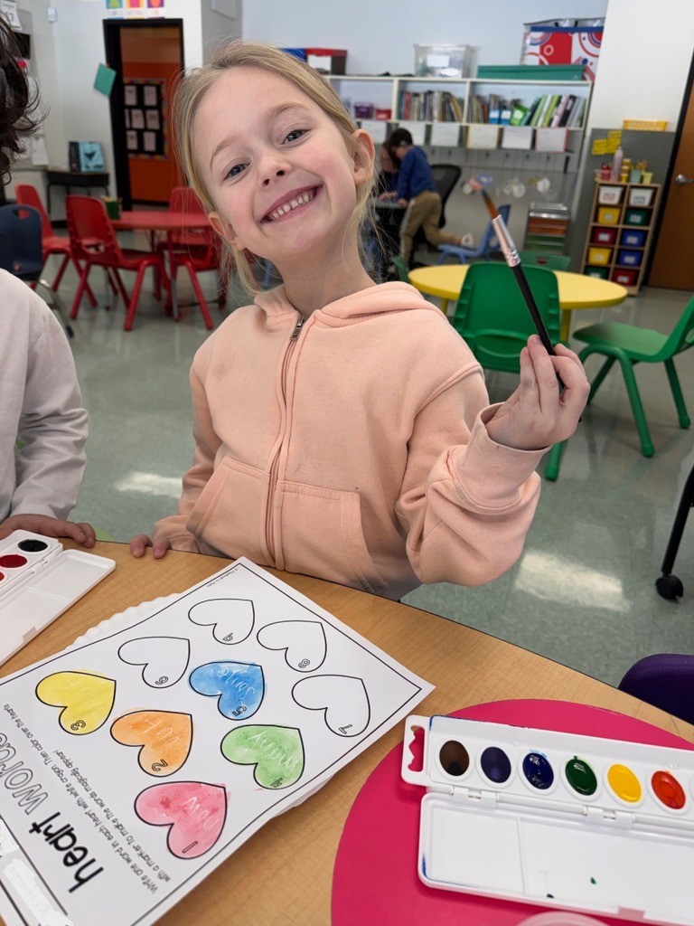 A student is seen with a paintbrush painting their "heart" words worksheet