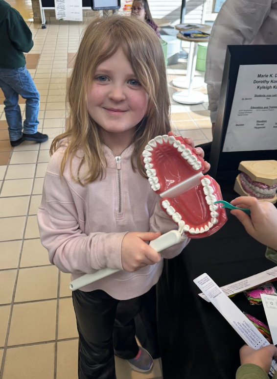 A student holds a model of a human mouth as she's being shown proper brushing and flossing methods