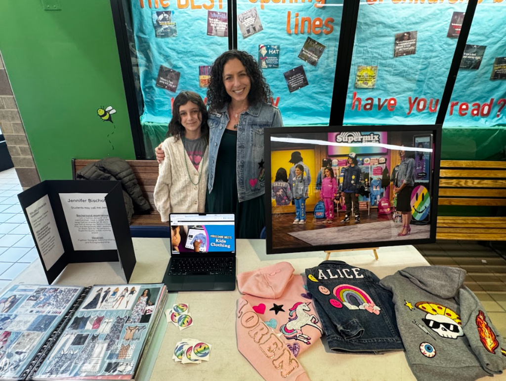 An adult poses with a child in front of a display representing fashion design