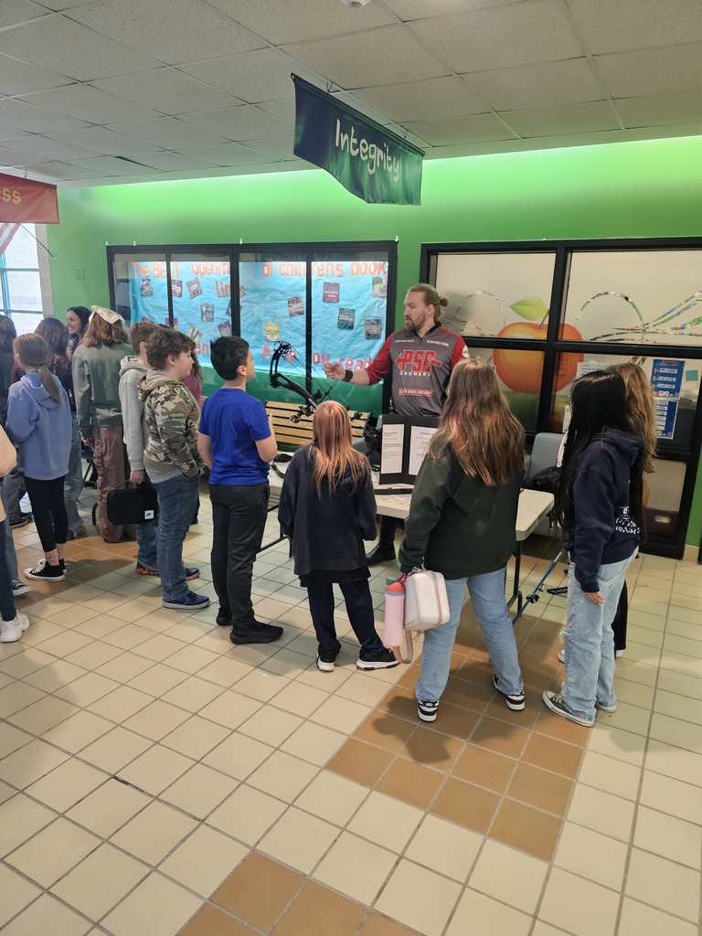 A group of students gather around a professional archer as he shows them his bow