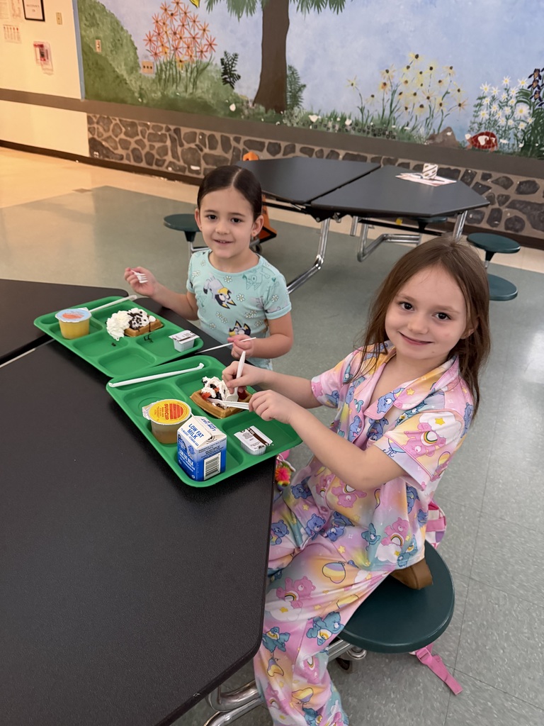 Two student sit at a cafeteria table with breakfast on their green trays.