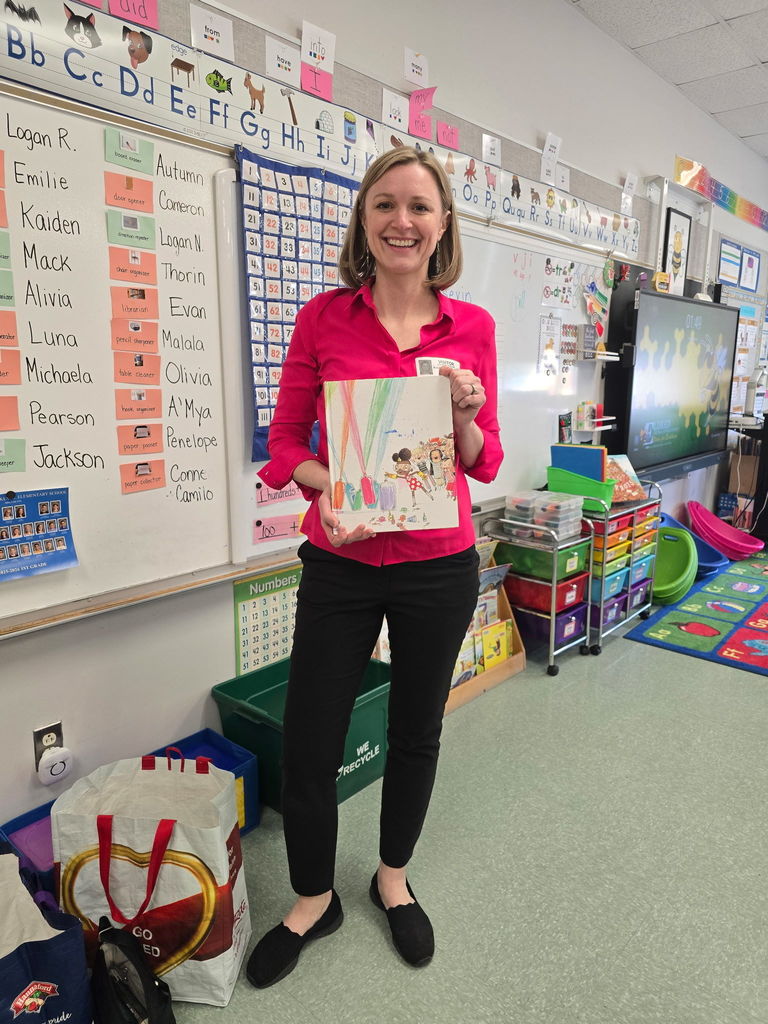 A parent came to read a book to our 1st grade class, she stands posing with the book "Ada Twist Scientist"