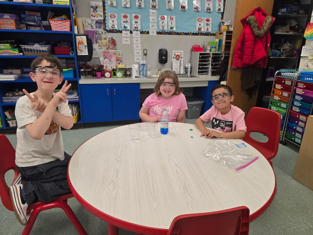 Students pose for the camera wearing safety goggles for a science experiment
