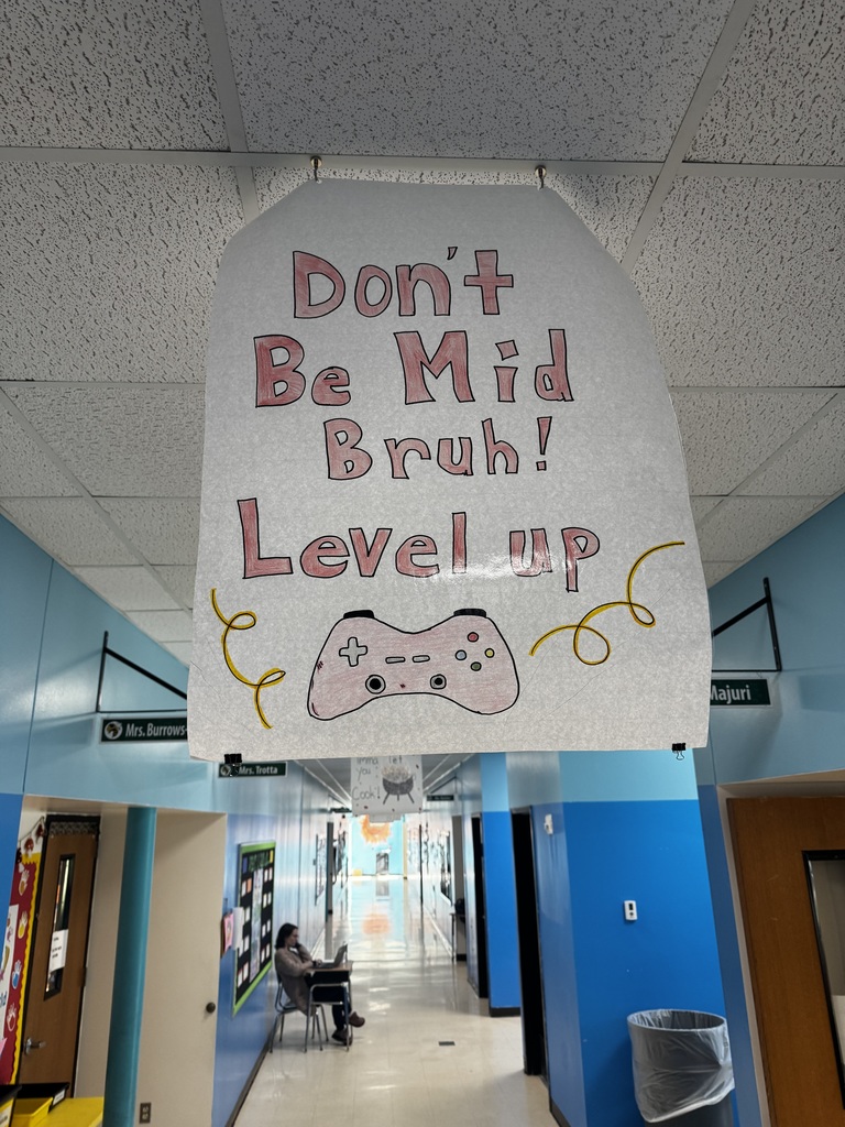 Image of a poster hanging from the ceiling of a school hallway that reads "Don't Be Mid Bruh! Level Up"