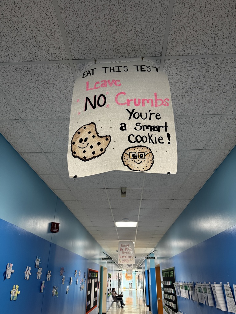 Image of a poster hanging from the ceiling of a school hallway that reads "Eat This Test, Leave No Crumbs, You're a Smart Cookie!"