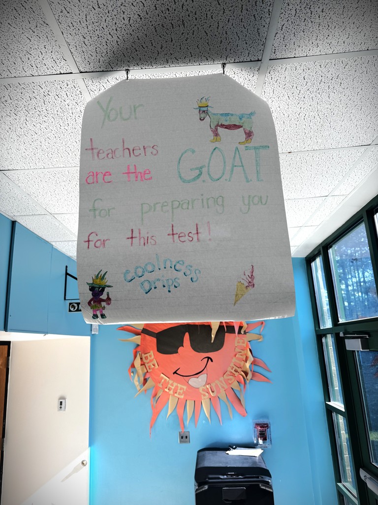 Image of a poster hanging from the ceiling of a school hallway that reads "Your teachers are the G.O.A.T for preparing you for this test! Coolness Drips"