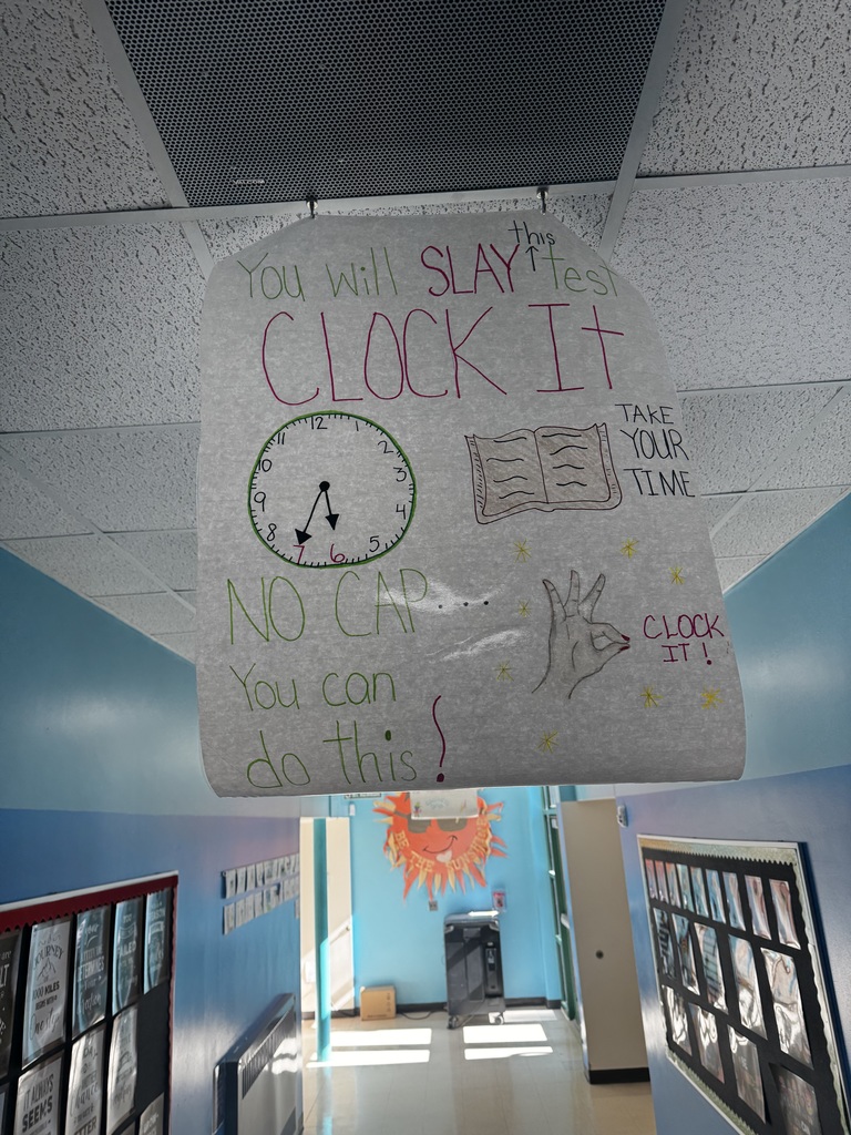 Image of a poster hanging from the ceiling of a school hallway that reads "You Will Slay This Test, Clock it, Take your Time, No Cap You Can Do This"