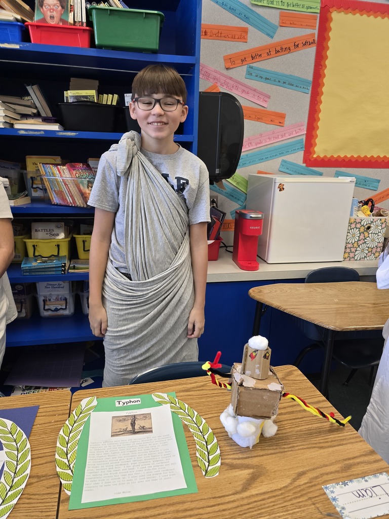 Image of a student in a toga made of a gray bed sheet standing behind his Greek Mythology project about Typhon