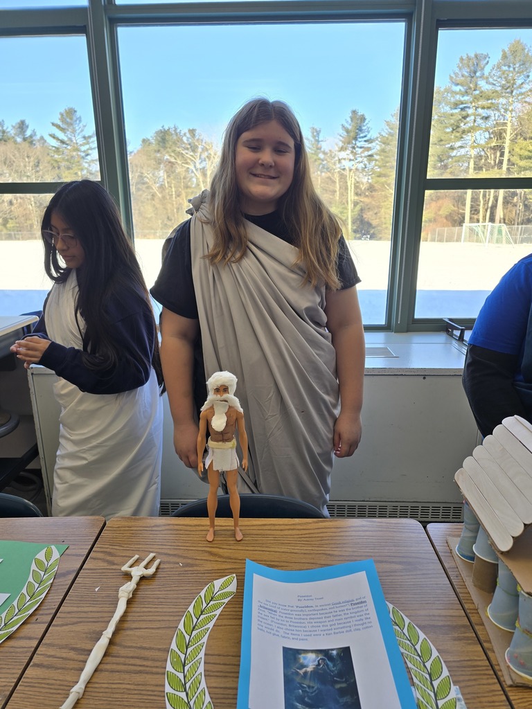Image of a student in a toga made of a gray bed sheet standing behind her Greek Mythology project about Poseidon