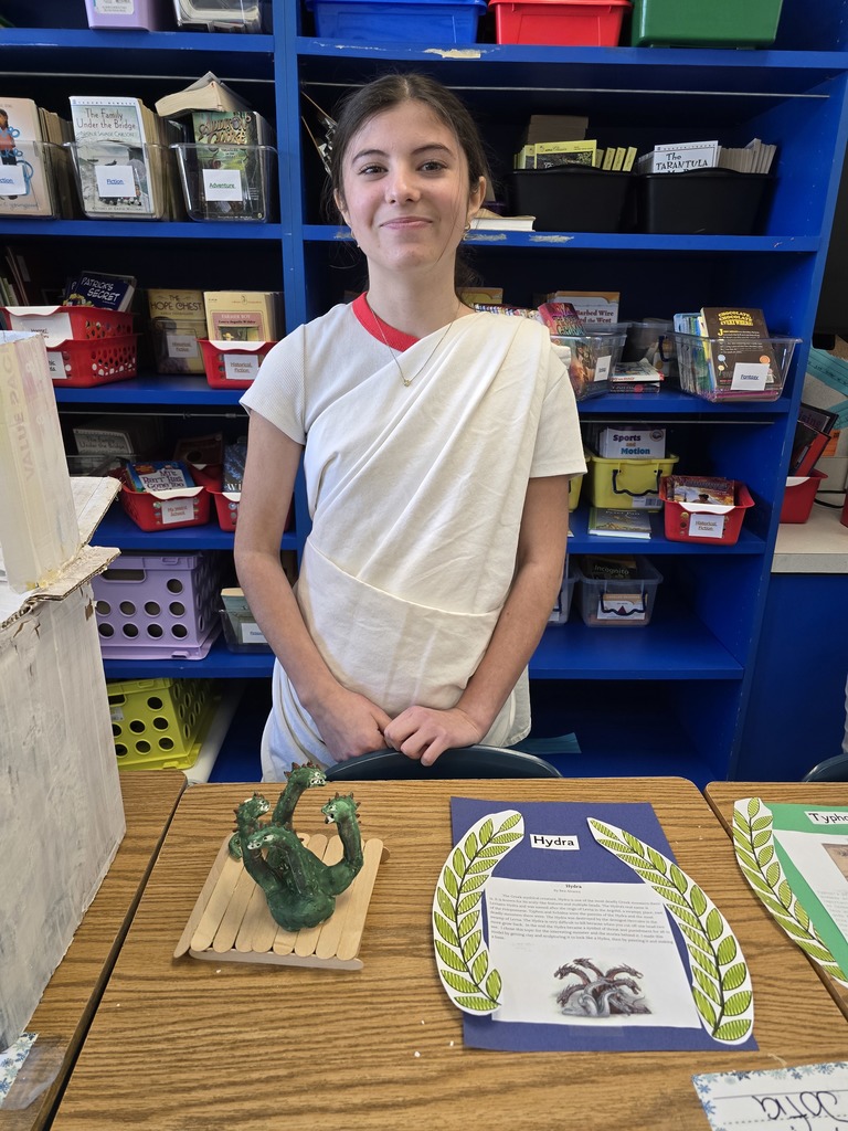 Image of a student in a toga made of a white bed sheet standing behind her Greek Mythology project about Medusa