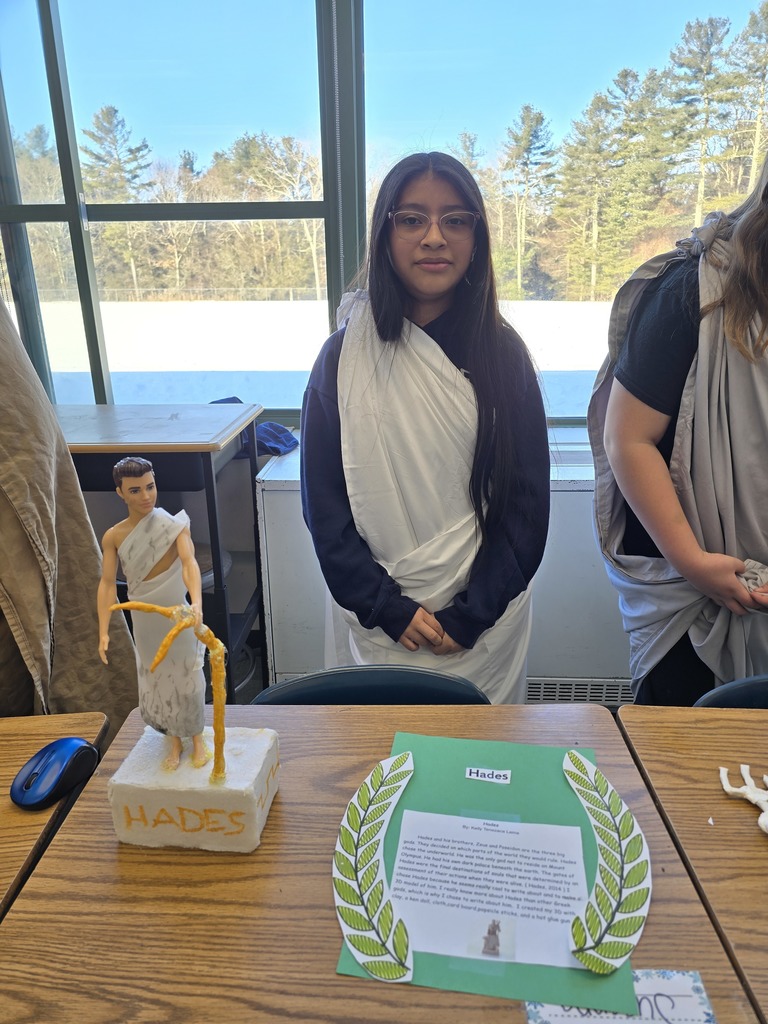 Image of a student in a toga made of a white bed sheet standing behind her Greek Mythology project about Hades