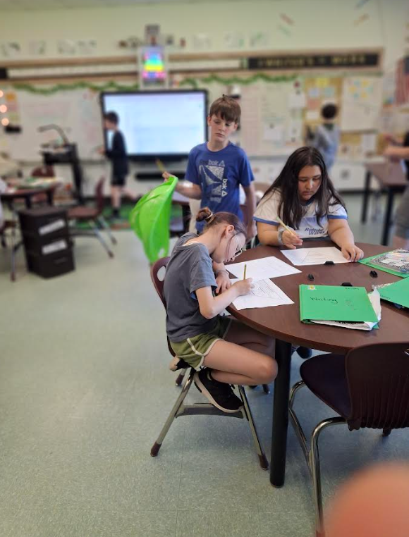 Image of students in a classroom, sitting at desks, working on a writing assignment