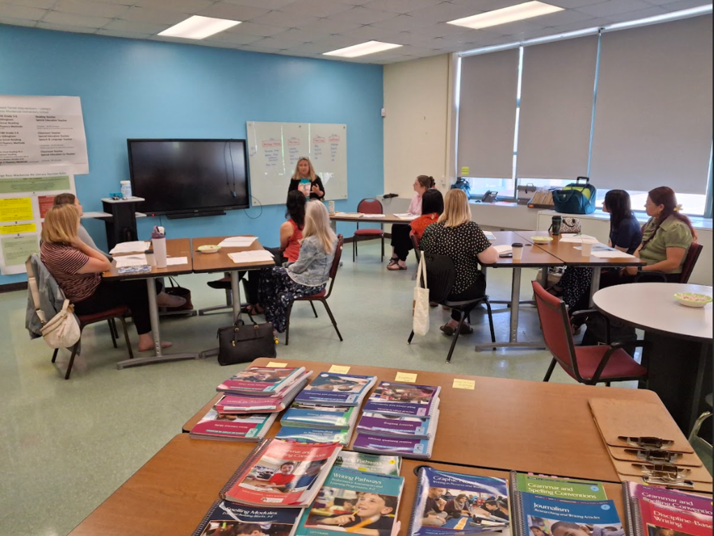 Image of educators sitting in a professional development session with a writing coach you can see the writing series of textbooks in the foreground