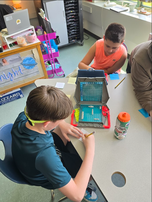 Image of students sitting at a table playing a game of Battleship