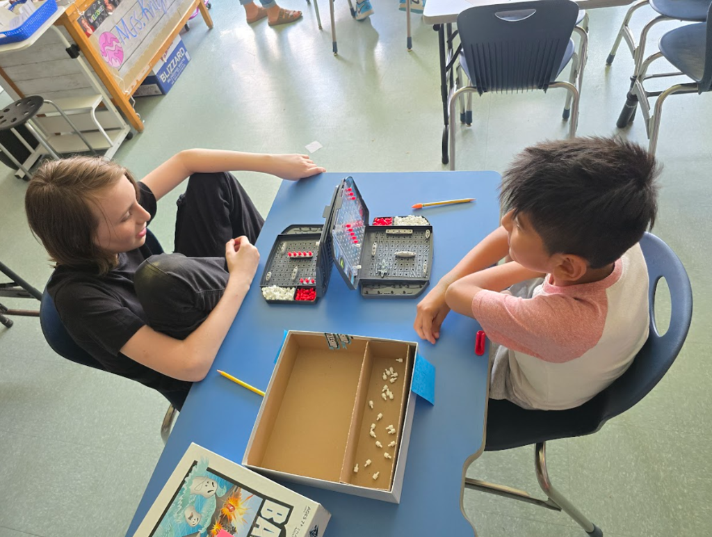 Image of students sitting at a table playing a game of Battleship