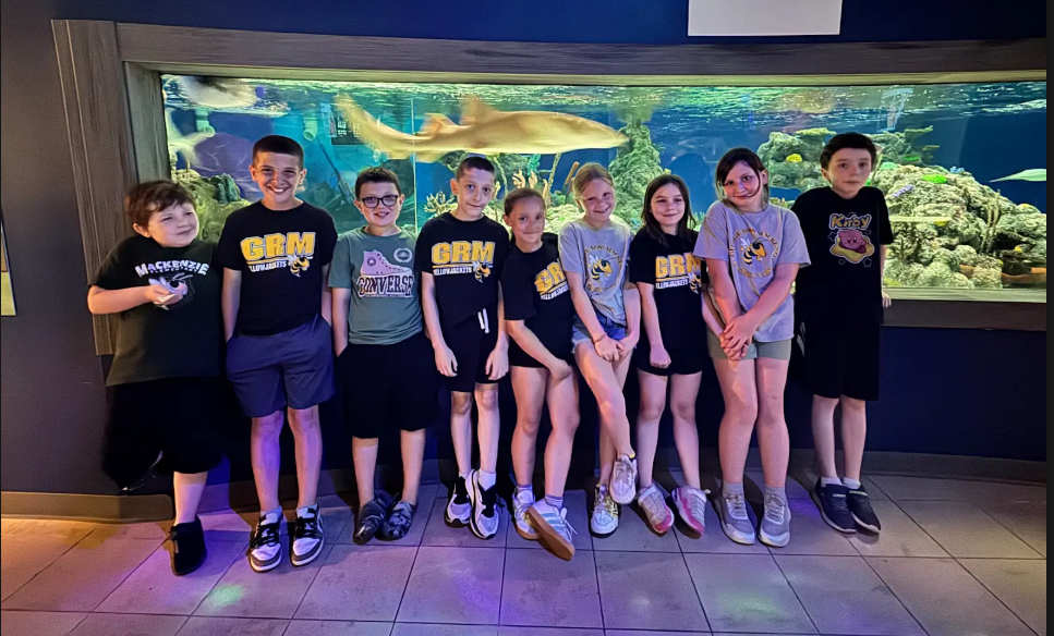 Students pose in from of a shark tank on a field trip to the aqluarium