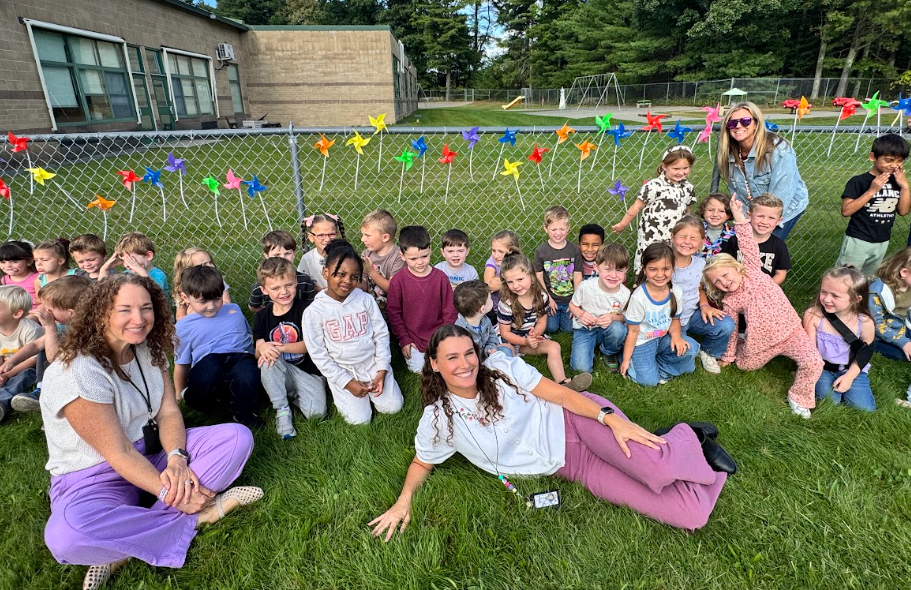 Image of students posing with their teachers in front of the pinwheels they placed in a fence to observe the annual International Day of Peace