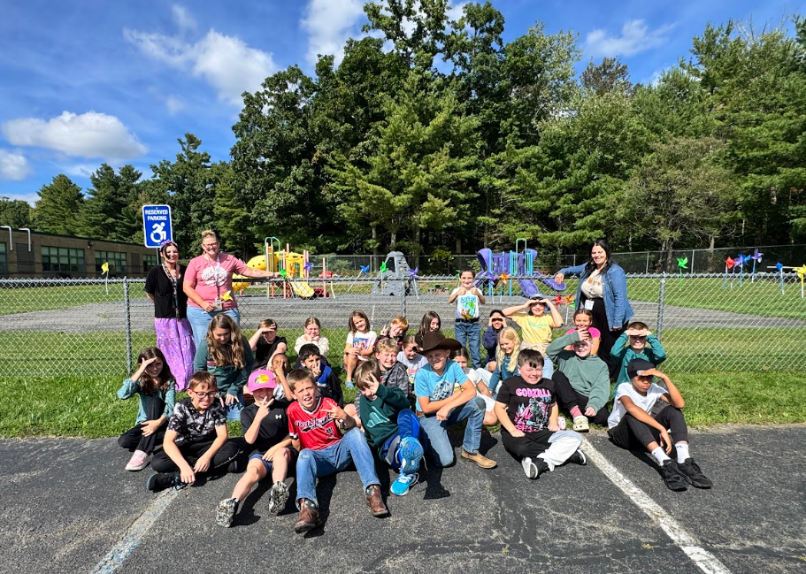 Image of students posing with their teachers in front of the pinwheels they placed in a fence to observe the annual International Day of Peace