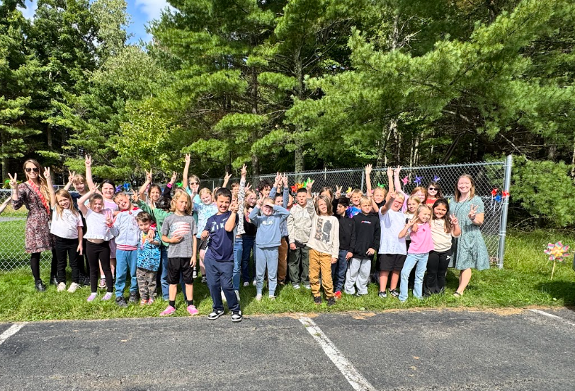 Image of students posing with their teachers in front of the pinwheels they placed in a fence to observe the annual International Day of Peace
