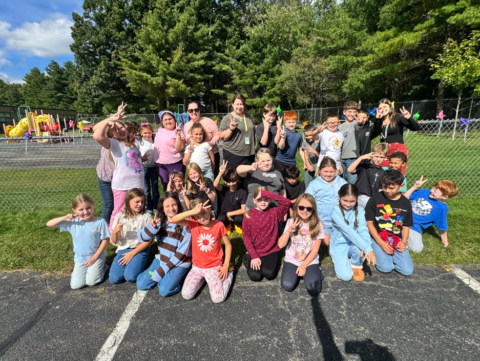 Image of students posing with their teachers in front of the pinwheels they placed in a fence to observe the annual International Day of Peace