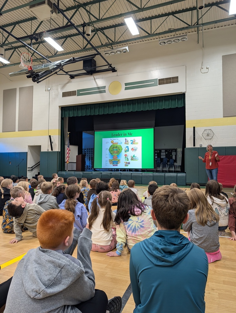 Image of students sitting on a gym floor listening to a grown up speak