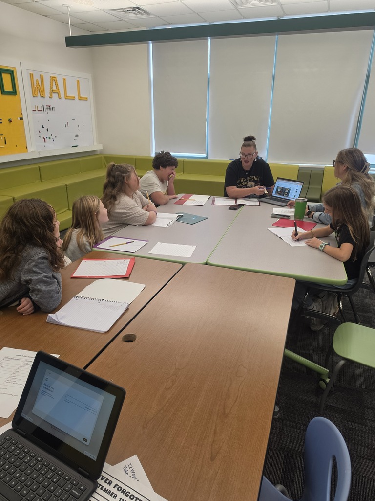 Students & adults sit at a table participating in a meeting