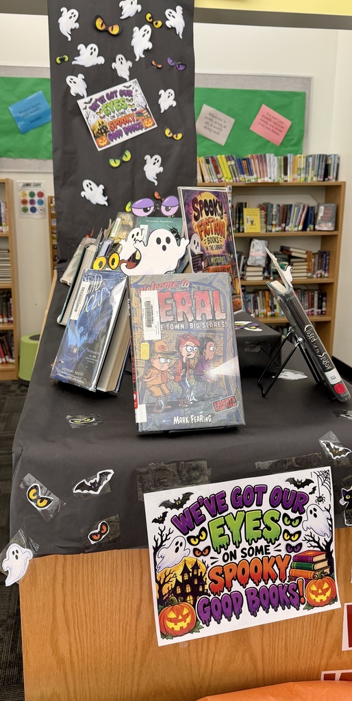 Image of a black paper runner hanging from the ceiling in a library that has ghosts and  eyeballs with Halloween books displayed. A sign is in the forefront that reads "we've got our eyes on some spooky good books!"