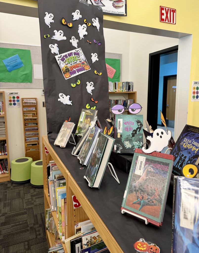 Image of a black paper runner hanging from the ceiling in a library that has ghosts and  eyeballs with Halloween books displayed