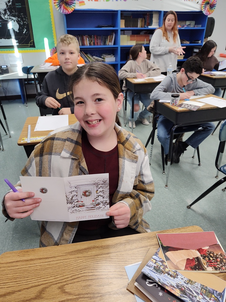 image of a student sitting at her desk holding up a holiday card she is sending to a member of the military